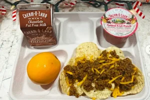 A typical school lunch tray with tacos, fruit, milk, and fruit cup served to students during lunch period. 